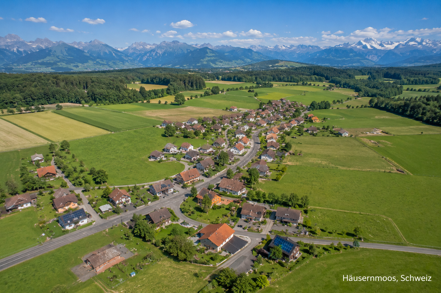 Luftaufnahme von Häusernmoos im Kanton Bern mit Dorf, Feldern und Alpenpanorama
